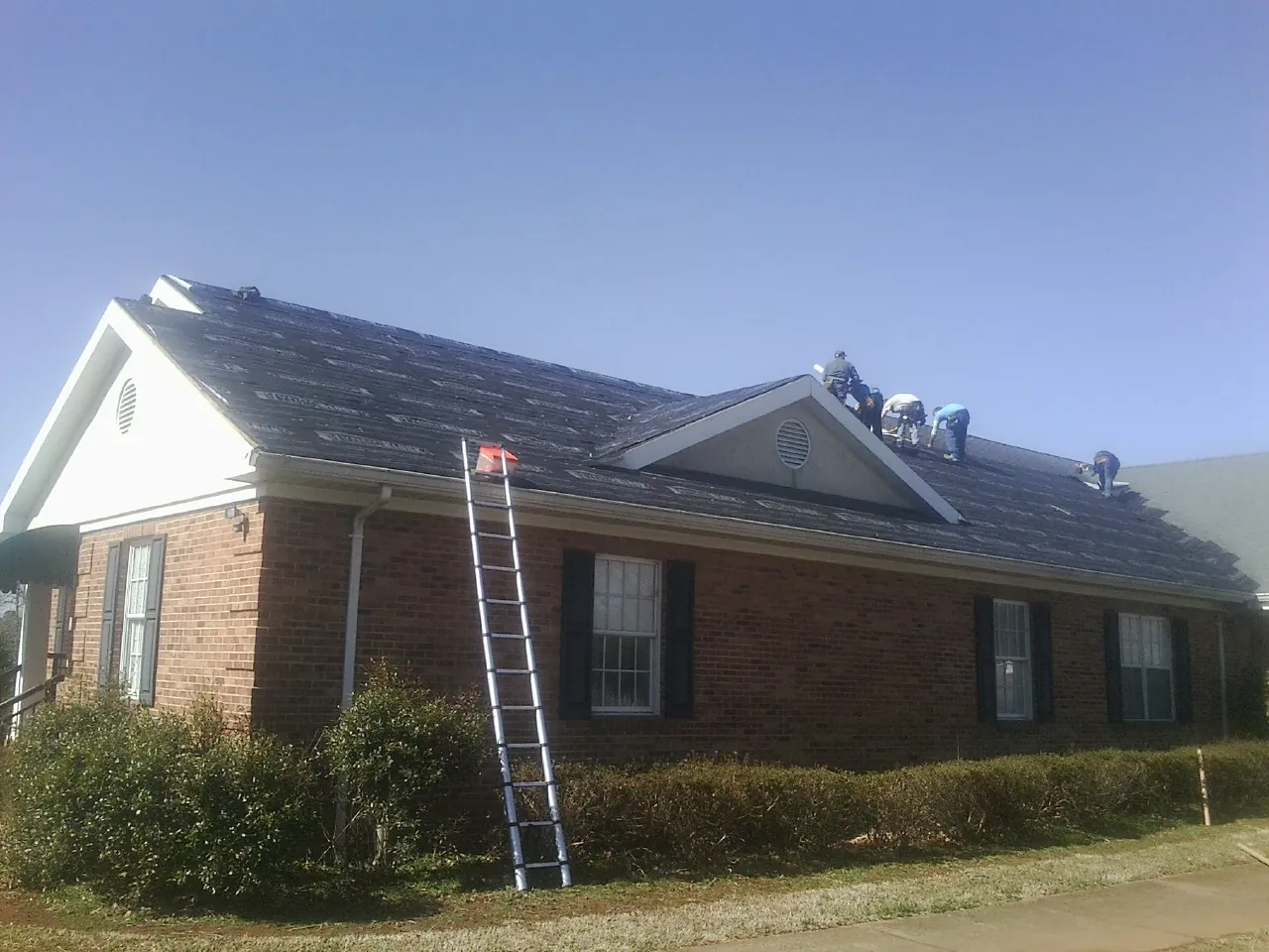 Crew tearing shingles off a brick ranch roof with a ladder set — Metal Roof Repair work by our crew in Anderson