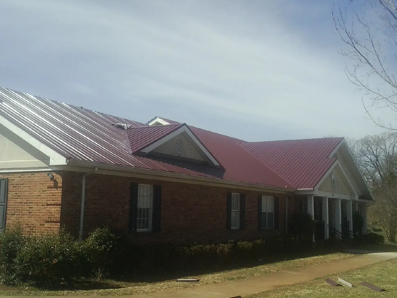 Red metal roof with gabled entries on a long brick building, from a Hail Damage Roof Repair job in Anderson