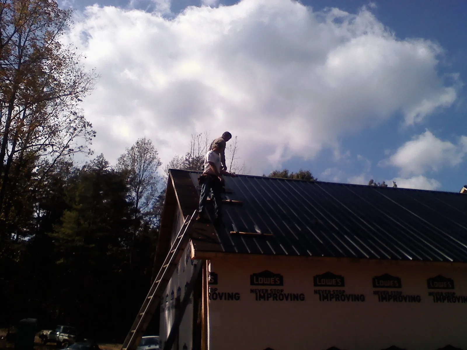 Roofer fastening dark metal panels high against a cloudy sky, from a Roof Inspection job in Anderson